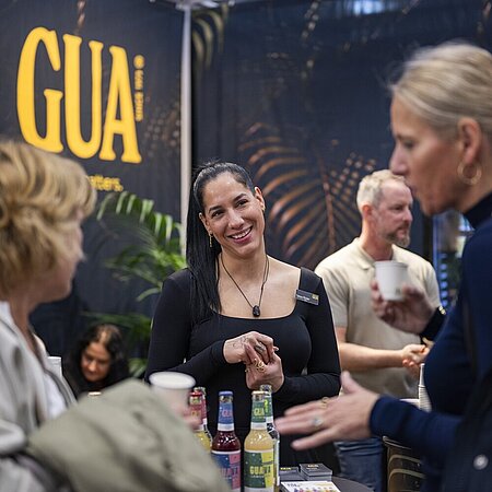 Messestand mit Getränken und Gesprächssituation vor einem GUA-Branding-Hintergrund.