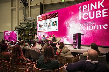 ine Panel-Diskussion auf der INTERNORGA-Bühne „PINK CUBE“. Mehrere Expertinnen und Experten sitzen auf der Bühne, während das Publikum in gemütlichen Sesseln zuhört. Eine große pinke LED-Wand zeigt das Thema der Diskussion.