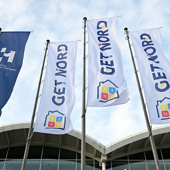Fahnen mit dem Logo der Messe GET NORD vor dem Eingangsbereich de Hamburg Messe unter blauem Himmel.
