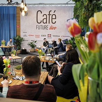 Eine inspirierende Gesprächsrunde im „Café Future live“ auf der INTERNORGA. Das Publikum sitzt an Tischen mit Blumen und Getränken, während auf der Bühne mehrere Personen über Branchenthemen diskutieren.